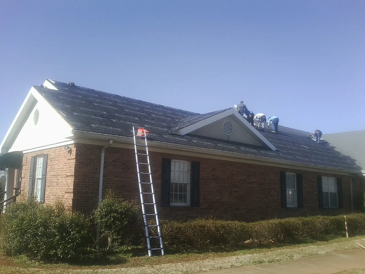 Crew tearing shingles off a brick ranch roof with a ladder set — Emergency Roof Repair work by our crew in Hyde Park
